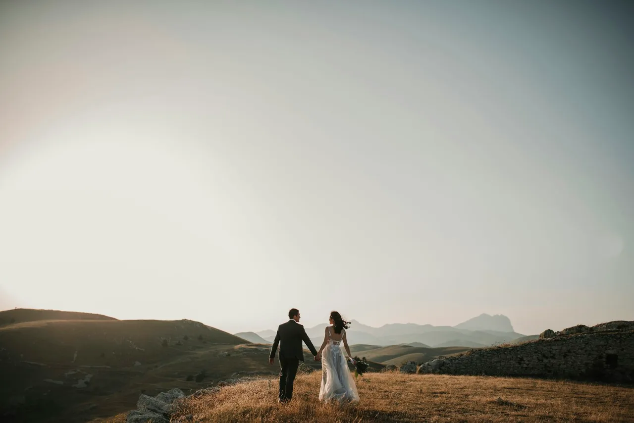 Gün batımında tepelerde el ele yürüyen gelin ve damat